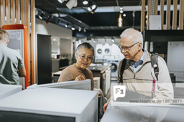 Ein älteres Ehepaar untersucht den Kühlschrank beim Einkaufen in einem Haushaltswarengeschäft
