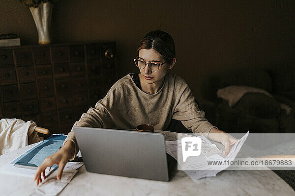 Nicht-binäre Person  die Rechnungen sammelt  während sie mit ihrem Laptop zu Hause sitzt