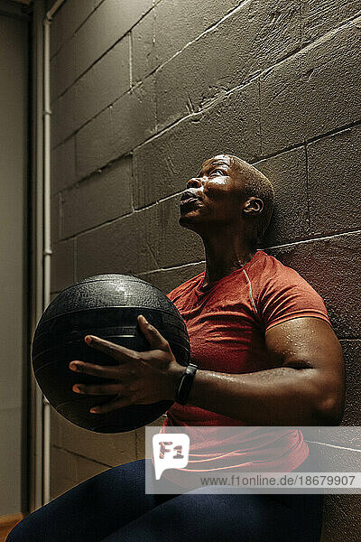 Engagierte Sportlerin  die einen Medizinball hält  während sie im Fitnessstudio eine Wandsitzübung macht