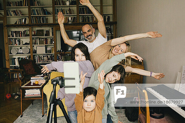 Glückliche Familie beim Filmen von Tänzen mit erhobenen Händen auf dem Smartphone zu Hause