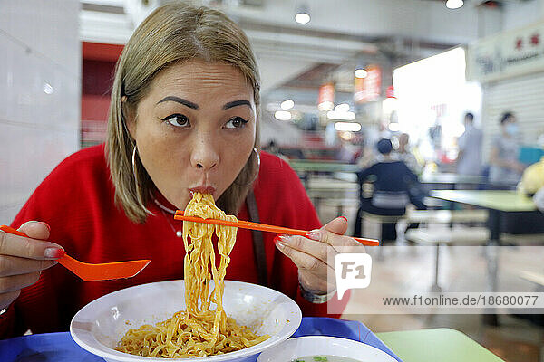 Young woman eating at traditional Asian food stall in Singapore Food Trail hawker center  Singapore  Southeast Asia  Asia