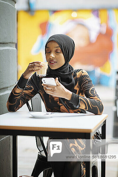 Young woman in hijab using phone in sidewalk cafe
