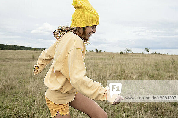 Smiling girl (10-11) in yellow beanie frolicking in field