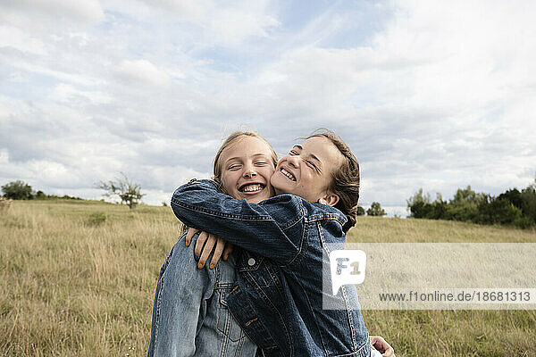 Smiling girl friends (10-11) hugging in field