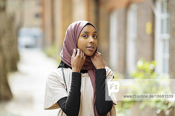 Portrait of young woman adjusting hijab