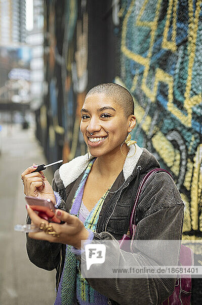 Portrait of hipster young woman applying lip gloss in street
