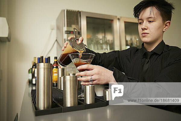 Young bartender preparing drink at bar