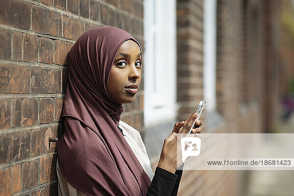 Portrait of young woman in hijab using phone