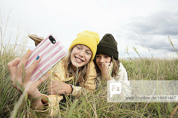 Smiling girl friends (10-11) lying in grass and taking selfie