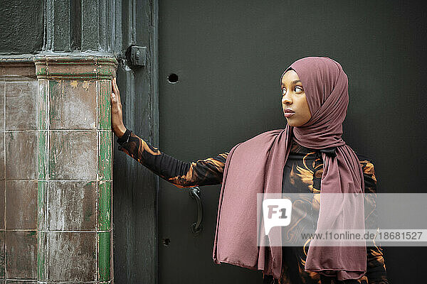 Young woman in hijab leaning against tiled wall