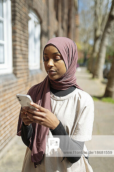 Young woman wearing hijab using phone in street