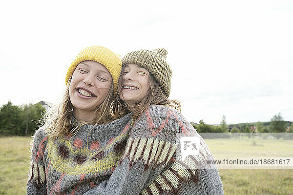 Smiling girl friends (10-11) wearing one sweater in field