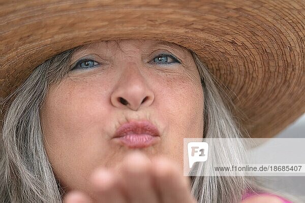 Nahaufnahme einer älteren Frau mit Hut  weißem Haar  blauen Augen und Sommersprossen  die der Kamera einen Kuss zuwirft