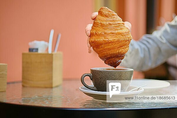 Unbekannte Frau dippt Croissant in Cappuccino auf der Außenterrasse