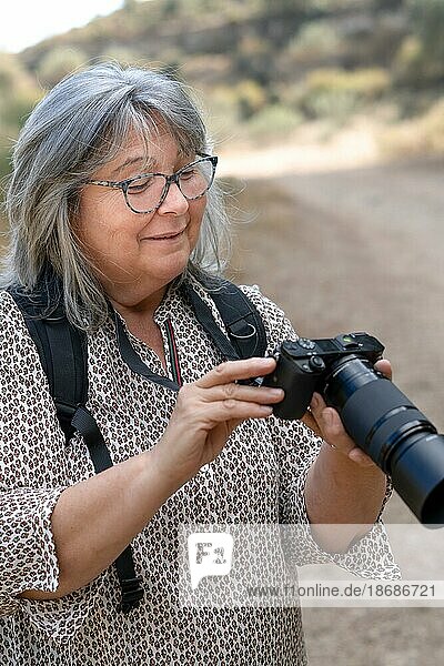 Older woman with white hair and glasses smiles as she looks at the pictures on her camera