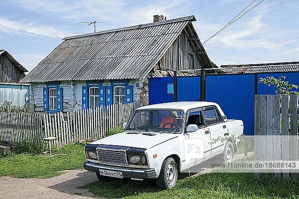 Traditionelles Holzhaus mit weißem Auto  Lada Riva  Lada Nova in einem ländlichen Dorf in Südsibirien  Russland  Europa