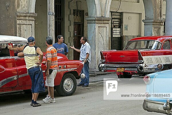 Kubanische Männer diskutieren auf der Straße und rote alte 1950er Jahre Oldtimer  Yank Tank in Old Havana  La Habana Vieja  Kuba  Karibik  Mittelamerika
