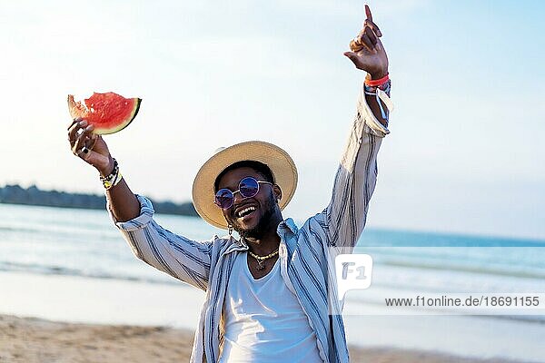 Schwarz ethnischen Mann genießen Sommerurlaub am Strand essen eine Wassermelone Spaß haben