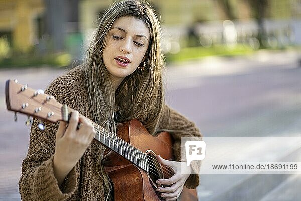Junge blonde Frau spielt Gitarre und singt auf der Straße