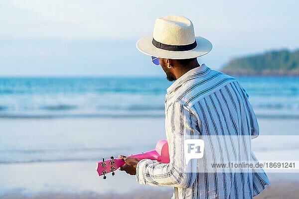 Porträt von schwarzen ethnischen Mann genießen Sommerurlaub am Strand spielen Ukulele am Meer