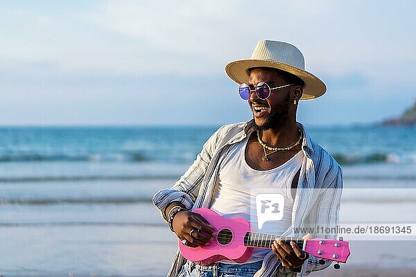 Porträt von schwarzen ethnischen Mann genießen Sommerurlaub am Strand spielen Ukulele