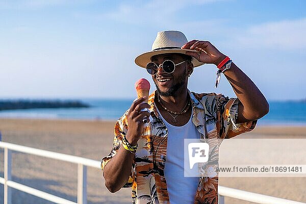 Black ethnic man enjoy summer vacation on the beach eating an ice cream having fun