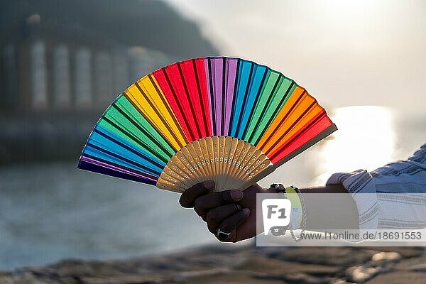 Stolz auf die LGBTQ Gemeinschaft. Hand mit gefälschten Nägeln in den Farben des Regenbogens hält Regenbogenfächer