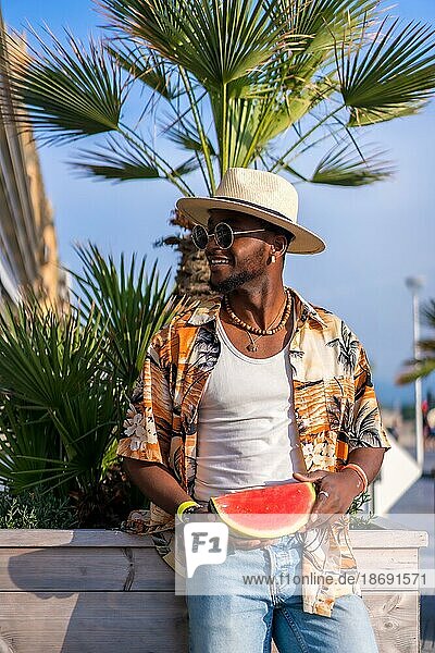 Porträt eines schwarzen ethnischen Mannes genießen Sommerurlaub am Strand  Schatten und eine Wassermelone lächelnd