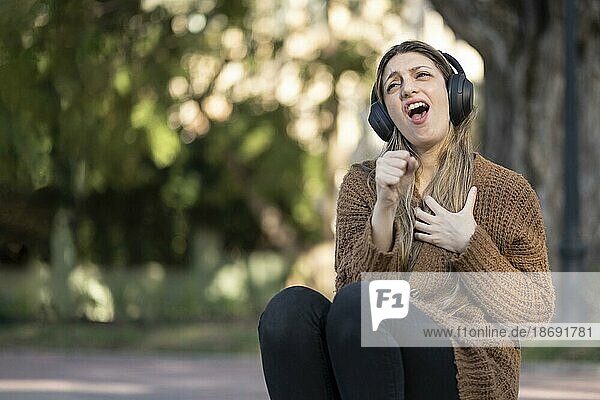 Blonde Frau sitzt auf der Straße  hört Musik und tut so  als hätte sie ein Mikrofon in der Hand und singt