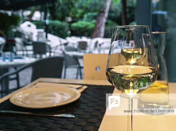Ein Glas und eine Karaffe Weißwein auf einem Tisch in einem Straßencafé und Geschirr  Geschirr und Besteck  selektiver Fokus und unscharfer Hintergrund. Essen im Freien im Sommer  Urlaub Mahlzeiten  Pause  Mittagszeit  Abendessen