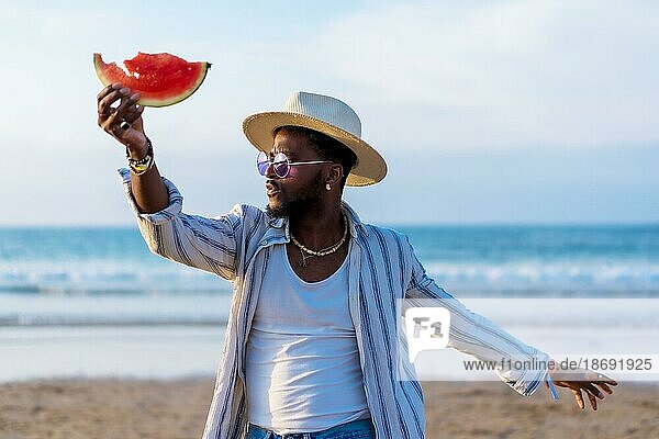Schwarz ethnischen Mann genießen Sommerurlaub am Strand essen eine Wassermelone am Meer