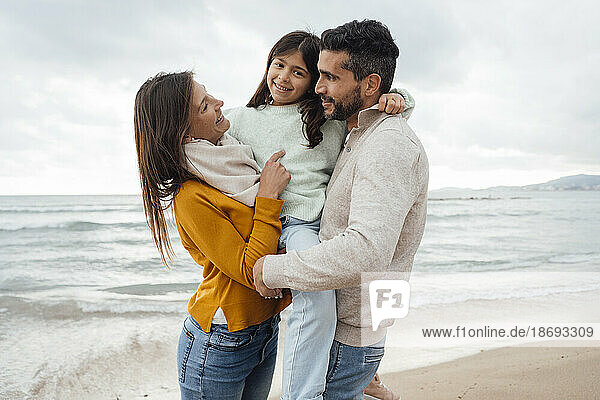 Happy woman standing with man and daughter on coastline at beach
