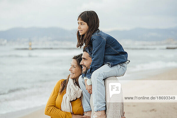 Smiling man and woman with daughter standing together at beach