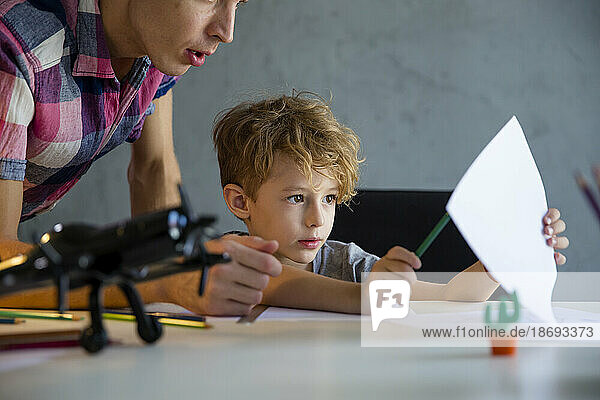 Father teaching son sitting at desk in home