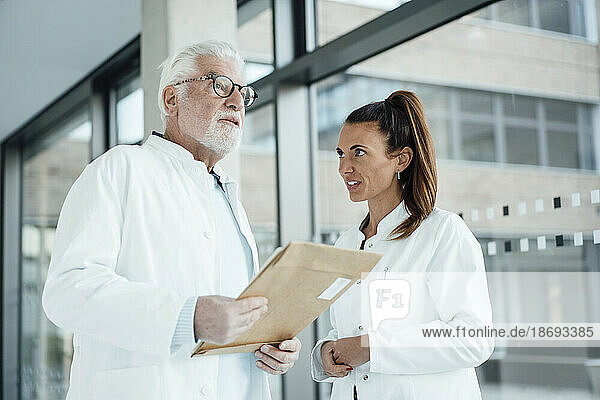 Senior doctor holding document and discussing with colleague in hospital