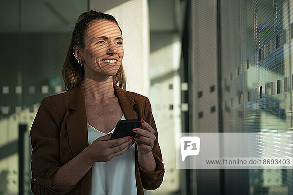 Happy businesswoman holding smart phone at office
