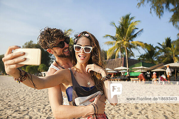 Woman taking selfie through smart phone with boyfriend at beach