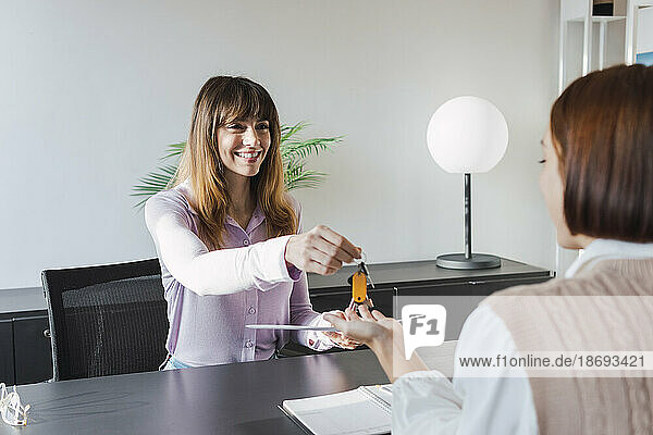 Happy real estate agent giving house keys to customer in office