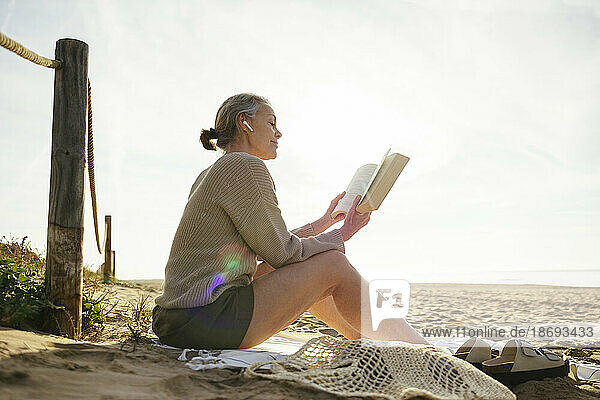 Mature woman reading book on sunny day at beach
