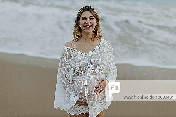 Happy pregnant woman standing at beach