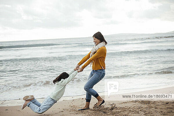 Happy woman spinning daughter at beach