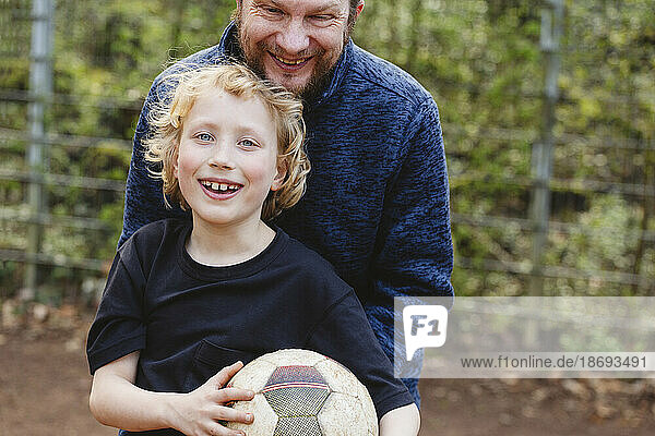 Father embracing happy son holding soccer ball