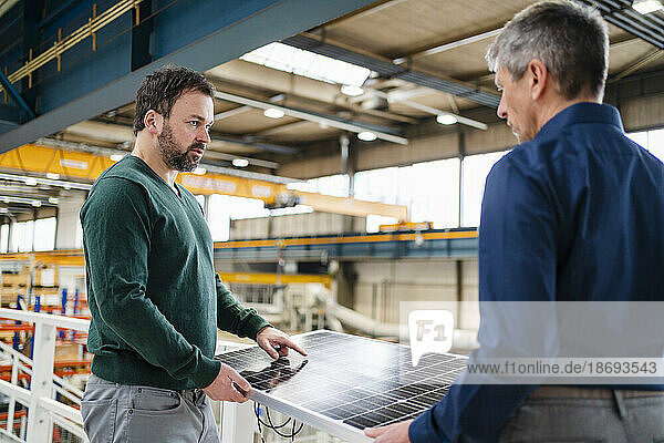 Manager discussing with businessman holding solar panel at factory