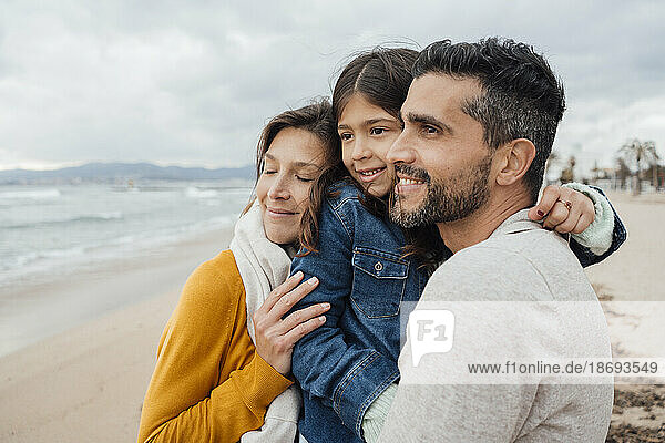 Lächelnde Frau mit Mann und Tochter  die sich am Strand umarmen