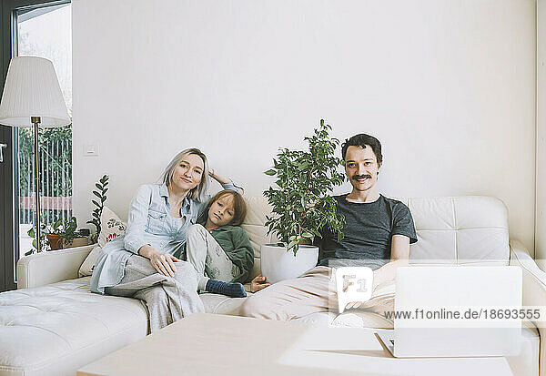 Smiling man and woman sitting on sofa with son at home