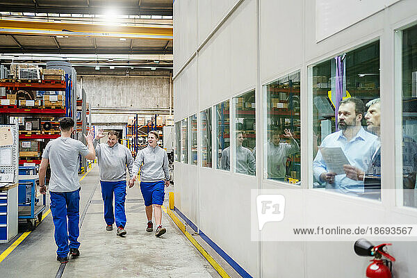 Happy colleagues giving high-five walking in production hall at factory