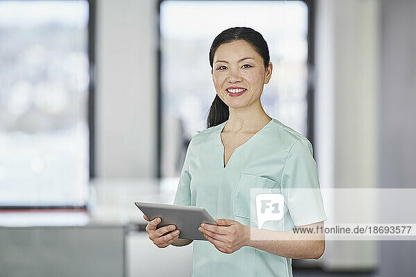 Portrait of smiling nurse in scrubs holding digital tablet