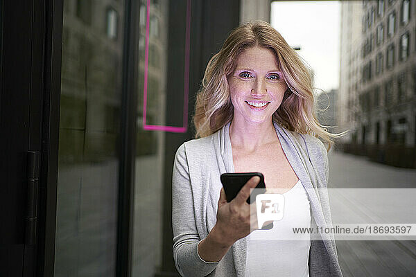 Smiling blond woman holding smart phone in hand