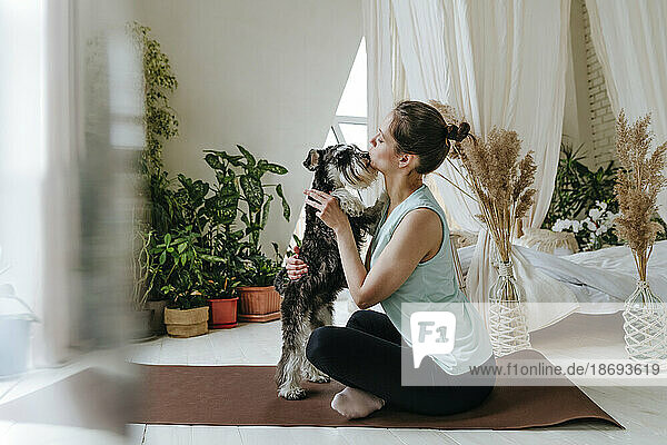 Woman spending leisure time with Schnauzer dog sitting on exercise mat at home