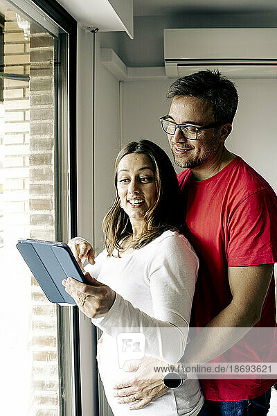 Woman showing tablet PC to man standing by window at home